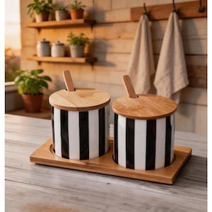 Op de afbeelding: Een witte keramische mok met een zwarte handgreep en de tekst "But First, Coffee" in een vetgedrukte, zwarte letter. De mok staat tegen een vage achtergrond, wat een gezellige omgeving suggereert.