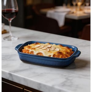 May include: A rectangular, blue ceramic baking dish filled with a baked casserole, topped with melted cheese and sliced almonds. A glass of red wine is in the background, on a white marble countertop.