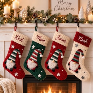 Peut inclure: Quatre chaussettes de Noël personnalisées suspendues en rangée. Les chaussettes sont rouges, vertes, rouges et crème, chacune avec un revers en tricot brodé des noms Dad, Mom, James et Noah. Chaque chaussette présente un gnome au bonnet rayé.