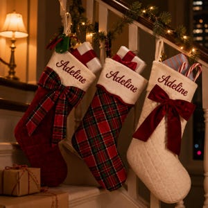 Peut inclure: Trois chaussettes de Noël suspendues à une rampe d'escalier. Chaque chaussette présente un revers blanc brodé du prénom Adeline en écriture rouge. Les chaussettes arborent des motifs écossais rouges, du tissu matelassé rouge et blanc.