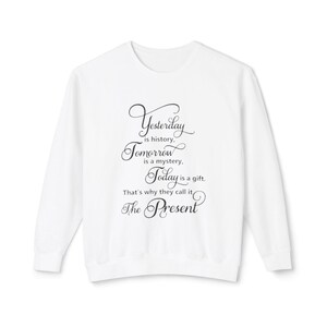 Könnte beinhalten: Ein weißes Sweatshirt mit langen Ärmeln. Auf der Vorderseite des Sweatshirts steht der Text "Yesterday is history, Tomorrow is a mystery, Today is a gift. That's why they call it, The Present" in schwarzer Schrift.