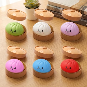 May include: A collection of colorful, dumpling-shaped objects with smiling faces, each nestled in a brown, round container with a lid. The dumplings are in various colors, including green, white, pink, blue, and red. The lids are a light brown color.