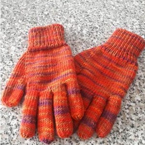 Puede incluir: Un par de guantes tejidos a mano en tonos naranja, rojo y morado. Los guantes tienen un puño acanalado y un patrón de rayas texturizado. Los dedos están bien definidos, lo que sugiere calidez y comodidad.