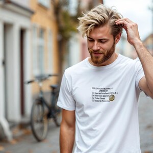 May include: White t-shirt with the text "DEPLOYMENT READINESS CHECKLIST" and a small graphic. The checklist includes items like "Runs on Localhost" and "Tested in Production". The shirt is worn by a person with blonde hair and a beard.