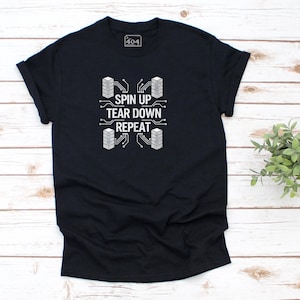 May include: A black t-shirt featuring the white text "SPIN UP TEAR DOWN REPEAT" and a circuit board design. The shirt has a crew neck and short sleeves. A small plant is in the background.