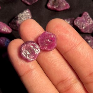 K&ouml;nnte beinhalten: Zwei kleine, rohe, tief pink-rote Rubin-Edelsteine mit unregelm&auml;&szlig;igen, facettierten Oberfl&auml;chen. Die Steine weisen eine nat&uuml;rliche, unpolierte Textur mit sichtbaren kristallinen Strukturen und verschiedenen Schattierungen von Magenta und Karmesinrot auf.