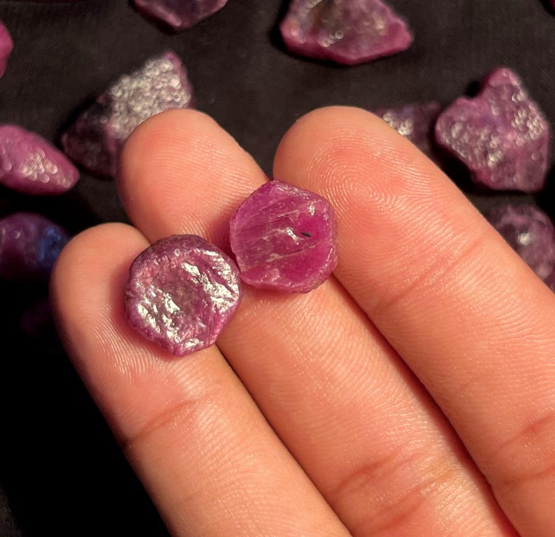 K&ouml;nnte beinhalten: Zwei kleine, rohe, tief pink-rote Rubin-Edelsteine mit unregelm&auml;&szlig;igen, facettierten Oberfl&auml;chen. Die Steine weisen eine nat&uuml;rliche, unpolierte Textur mit sichtbaren kristallinen Strukturen und verschiedenen Schattierungen von Magenta und Karmesinrot auf.