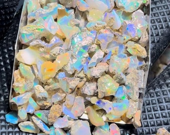 Könnte beinhalten: Ein Tablett voller roher Opal-Edelsteine. Die Opale zeigen eine Vielzahl von Farben, darunter Blau, Grün, Gelb und Orange, mit schillernden Blitzen. Die rohen Steine haben ein natürliches, unpoliertes Aussehen.