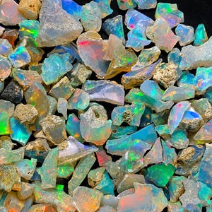 Könnte beinhalten: Eine Sammlung roher, unpolierter Opalsteine mit einer durchscheinenden, milchig-weißen Basis und lebhaften Blitzen aus irisierendem blauem, grünem und orangefarbenem Licht. Die Steine sind unregelmäßig geformt und zeigen natürliche Texturen.
