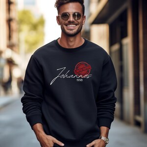 Könnte beinhalten: Ein schwarzes Sweatshirt mit Rundhalsausschnitt und dem Namen "Johannes" in weißer Schrift. Ein roter runder Stempel zeigt "Limited Edition" über dem Jahr "1998". Das Sweatshirt wird von einer Person getragen.