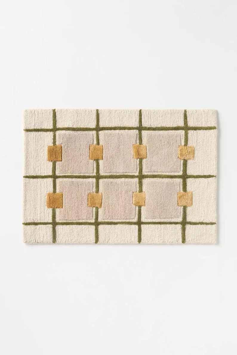 Puede incluir: Alfombra rectangular crema con un dise&ntilde;o de cuadr&iacute;cula. Las l&iacute;neas de la cuadr&iacute;cula son verde oliva y los cuadrados son de color rosa claro. Las intersecciones de la cuadr&iacute;cula tienen peque&ntilde;os acentos cuadrados de color amarillo dorado.
