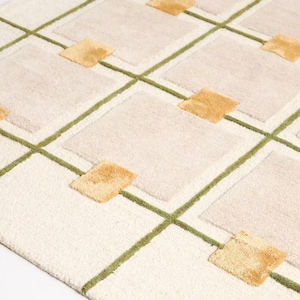 Puede incluir: Alfombra color crema con un patr&oacute;n geom&eacute;trico. El dise&ntilde;o presenta cuadrados en beige y dorado, delineados con l&iacute;neas verdes. La alfombra tiene una superficie texturizada, agregando profundidad al dise&ntilde;o.