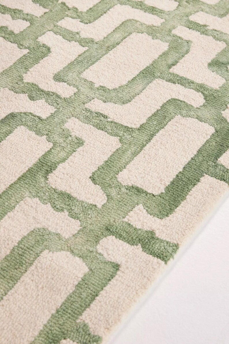 May include: Close-up of a rug with a geometric pattern. The rug has a repeating design of light green shapes against a cream background. The texture appears soft and plush, suggesting a comfortable floor covering.