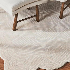 May include: A cream-colored rug with a wavy pattern and a scalloped edge. Two white upholstered benches with wooden legs are partially visible. The rug is on a hardwood floor.