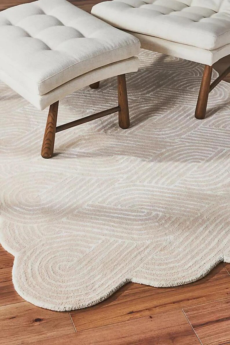 May include: A cream-colored rug with a wavy pattern and a scalloped edge. Two white upholstered benches with wooden legs are partially visible. The rug is on a hardwood floor.