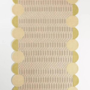 May include: A rectangular rug with a textured, beige central design and a border of alternating beige circles and olive-green half-circles. The rug's pattern features vertical and diagonal lines.