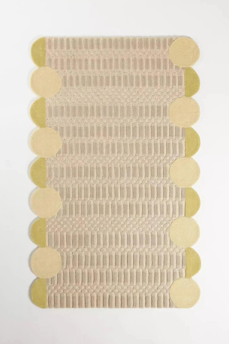 May include: A rectangular rug with a textured, beige central design and a border of alternating beige circles and olive-green half-circles. The rug's pattern features vertical and diagonal lines.