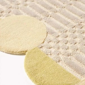 May include: Close-up of a beige and light green rug with a geometric design. The rug features a textured pattern with circular and semi-circular shapes in light green and beige, set against a background of beige and gray stripes.
