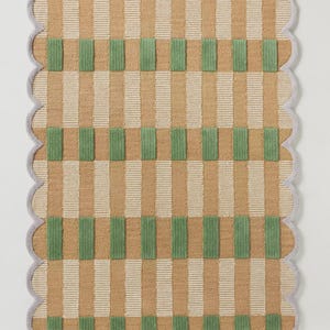 May include: A rectangular rug with a scalloped edge. The rug features a pattern of vertical stripes in tan and white, with green rectangular blocks. The border is a light gray color.