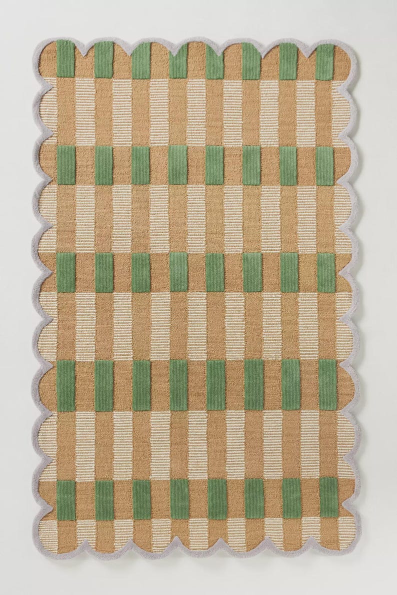 May include: A rectangular rug with a scalloped edge. The rug features a pattern of vertical stripes in tan and white, with green rectangular blocks. The border is a light gray color.