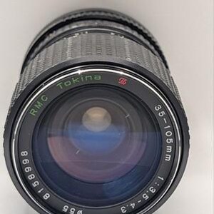 May include: A black Tokina RMC 35-105mm 1:3.5-4.3 camera lens with a 55mm filter diameter. The front element is dark with blue-tinted glass. The lens barrel features a textured rubber grip ring and white printed text detailing the specifications.