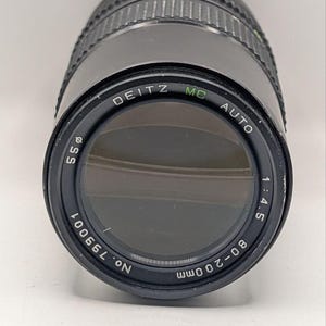 May include: A black Deitz MC Auto 80-200mm camera lens with a 55mm filter diameter. The front element is dark, and the outer ring features the text 'DEITZ MC AUTO 1:4.5 80-200mm No. 799001' printed in white around the glass perimeter.