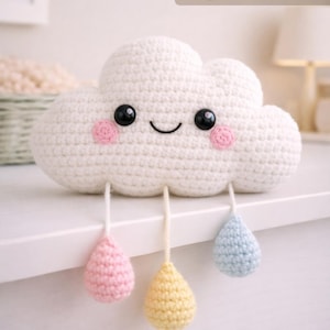 Könnte beinhalten: Eine gehäkelte weiße Wolke mit schwarzen Augen, rosa Wangen und einem lächelnden Mund. Drei Tränen in Rosa, Gelb und Blau hängen darunter. Der Text "PDF Pattern Digital Download" befindet sich in der oberen rechten Ecke.