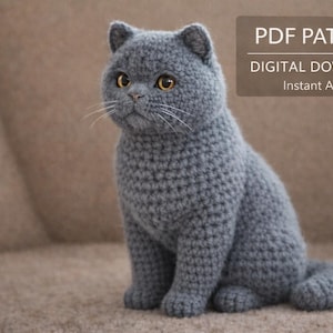 Può includere: Un gatto grigio all'uncinetto con occhi gialli è seduto su una superficie marrone. Il gatto è fatto di filato e ha una consistenza dettagliata. Il testo in alto a destra recita "PDF PATTERN DIGITAL DOWNLOAD Instant Access."