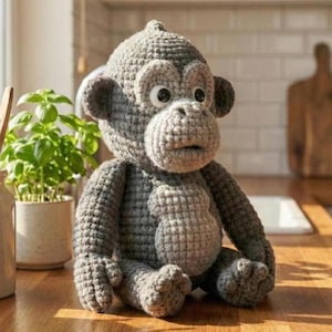 Könnte beinhalten: Eine handgefertigte, graue Häkelaffenpuppe mit großen, ausdrucksstarken Augen und einem detaillierten, strukturierten Design. Das Stofftier sitzt auf einer Holzoberfläche und zeigt seine Arme, Beine und seinen Bauch. Der Affe hat einen kleinen Kopf und große Ohren.
