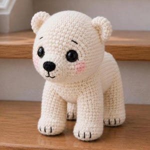 May include: A handmade, off-white crochet polar bear toy. The bear has black eyes, a black nose, and pink cheeks. It is standing on all fours, with small black stitches for claws.