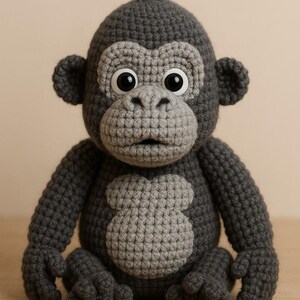 Puede incluir: Un peluche de gorila hecho a mano con ganchillo en tonos grises. El gorila tiene ojos grandes y expresivos, una cara, pecho y manos de color gris claro. El peluche est&aacute; sentado con los brazos y las piernas extendidos, mostrando el detallado trabajo de ganchillo.