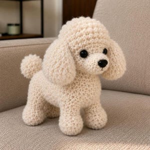 Puede incluir: Un perro caniche de ganchillo color crema con ojos y nariz negros. El animal de peluche hecho a mano tiene orejas grandes y caídas y una cola esponjosa. El caniche está de pie sobre sus cuatro patas, mostrando su detallada textura de ganchillo.