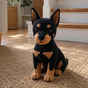May include: A handcrafted crochet dog figurine featuring a black and tan color scheme. The plush toy has pointed ears, dark eyes, and a textured yarn surface, depicted in a seated position with detailed stitching visible across its entire body.