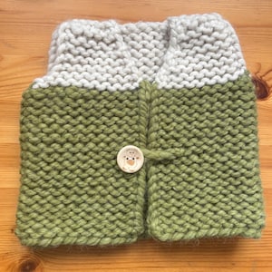 Puede incluir: Un chaleco de bebé tejido a mano en verde oliva y gris claro. El chaleco presenta un botón redondo de madera con un diseño de oso. La construcción de punto grueso proporciona una apariencia acogedora y texturizada. El chaleco está diseñado para mantener al bebé abrigado.