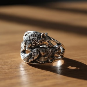 Peut inclure: Une bague en argent représentant deux loups détaillés. Les loups sont finement conçus, avec une fourrure texturée et des traits expressifs. La bague est une pièce maîtresse, mettant en valeur un design inspiré de la nature.