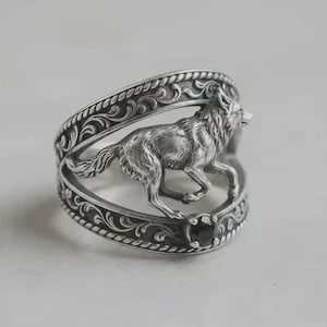 Peut inclure: Bague argentée ornée d'un loup courant finement détaillé. La bague présente un motif ajouré avec des volutes décoratives et un accent de pierre noire. Le loup est sculpté de manière réaliste, ajoutant une touche d'élégance inspirée de la nature.