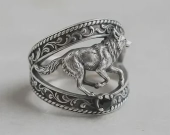 May include: A silver-colored ring featuring a detailed running wolf design. The ring has an openwork band with ornate scrollwork and a black gemstone accent. The wolf is sculpted in a realistic style, adding a touch of nature-inspired elegance.