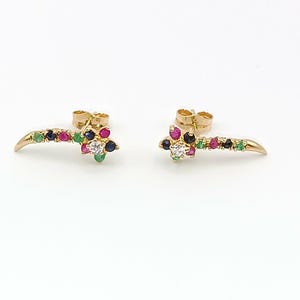 Peut inclure: Une paire de boucles d'oreilles dorées. Chaque boucle d'oreille présente un groupe de pierres précieuses colorées, dont des pierres rouges, vertes, bleues et une pierre centrale transparente. Les boucles d'oreilles ont un design incurvé et allongé.