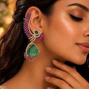 May include: An ear cuff earring featuring a curved row of marquise-cut pink stones, a small oval green stone, and a large pear-shaped green stone drop. The design is accented with small clear stones set in a gold-toned metal frame.