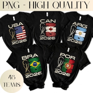 May include: Five black t-shirts featuring a graphic design with the text 2026, a trophy icon, and country abbreviations including USA, CAN, ARG, BRA, and POR. Each shirt displays a distressed national flag pattern within the number 26.