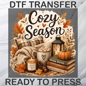 May include: A DTF transfer ready to press featuring the text Cozy Season, a plaid pillow, a knit blanket, a mug with a heart, a candle labeled Hello Fall, a lantern, a pumpkin, and books titled Sweater Weather, Crunchy Leaves, and Warm & Cozy.