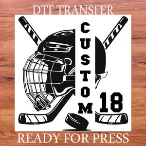May include: Black and white DTF transfer design featuring a hockey helmet, sticks, and a puck. The word "CUSTOM" is vertically displayed, along with the number "18". The text "READY FOR PRESS" is at the bottom.