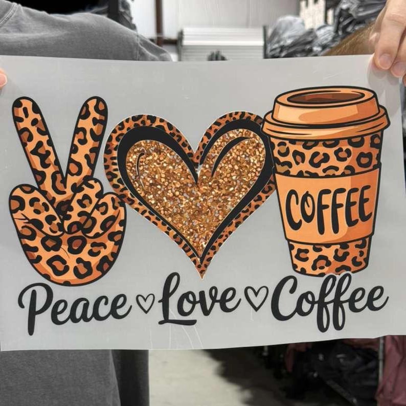 May include: A white rectangular transfer sheet featuring a leopard print peace sign, a glittery gold heart, and a leopard print coffee cup. Below the graphics, the black text reads Peace, Love, and Coffee, separated by small black heart icons.