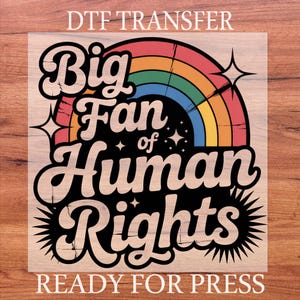 May include: A DTF transfer with the text "Big Fan of Human Rights" in a retro font, featuring a rainbow and starburst design. The words "Ready for Press" are at the bottom. The design is on a wooden background.