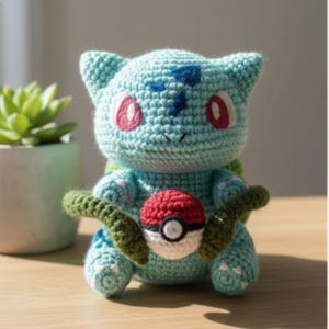 May include: Crocheted Bulbasaur plush toy in shades of blue, green, red, and white. The handmade toy features a red and white Pokeball and green vines. The Bulbasaur has pink eyes and blue markings. The plush is sitting on a wooden surface.
