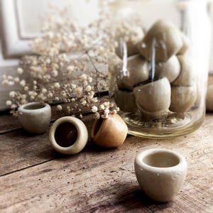May include: Five small ceramic pots in various shades of beige and brown. The pots are arranged on a rustic wooden surface.