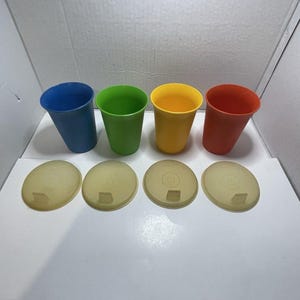Può includere: Quattro bicchieri di plastica colorati in blu, verde, giallo e rosso, con coperchi abbinati. I bicchieri sono disposti in fila, mostrando le loro tonalità vivaci. I coperchi sono giallo traslucido.
