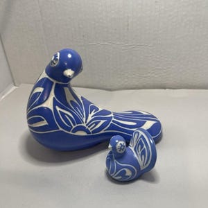 May include: Two ceramic bird figurines in a vibrant blue color with white floral and leaf patterns. The larger bird is positioned on the left, while a smaller bird figurine with a similar blue and white design is placed to its right.