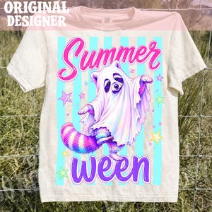 Op de afbeelding: Een crèmekleurig t-shirt met een afbeelding van een wasbeer verkleed als spook onder een wit laken. Het ontwerp bevat de tekst Summer ween in roze en paars, tegen lichtblauwe verticale strepen en kleine kleurrijke sterren rond de wasbeer.
