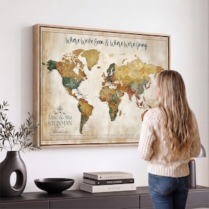 May include: A framed world map wall art piece with a vintage-style parchment background. The map features the text "Where We've Been & Where We're Going" at the top and "Jane & Stu STEINMAN" with a compass icon on the lower left side.